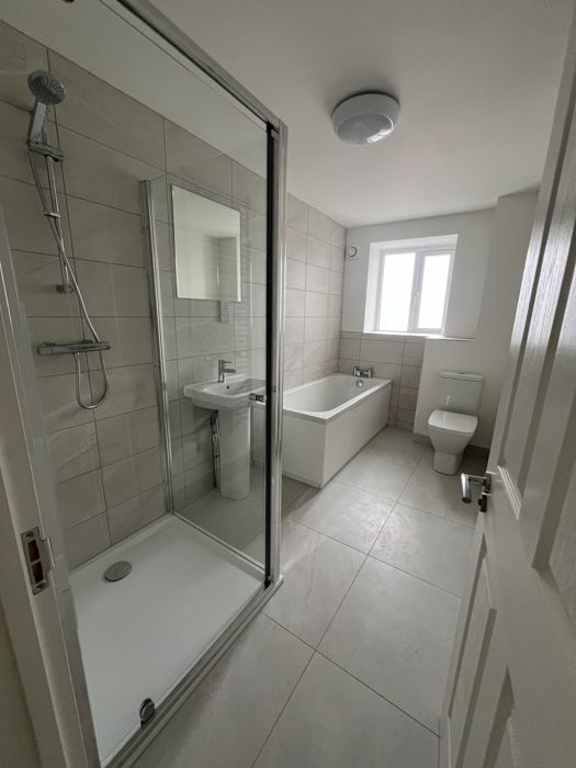 After: finished bathroom with walk-in shower, bath, basin and toilet in light stone-effect tiles