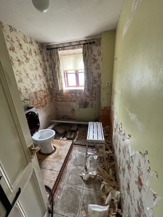 Before: old bathroom stripped back with floral wallpaper peeling off, a raised floor and an old toilet