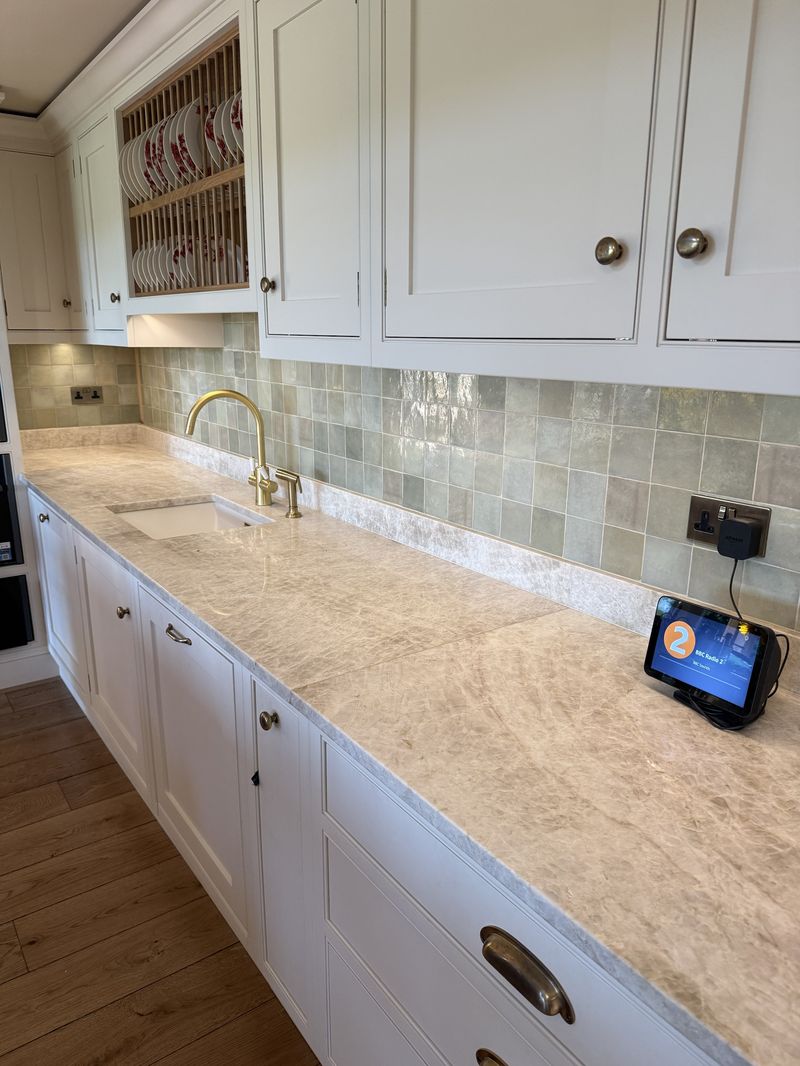 Kitchen with sage splashback tiles, stone worktop and a brushed brass tap