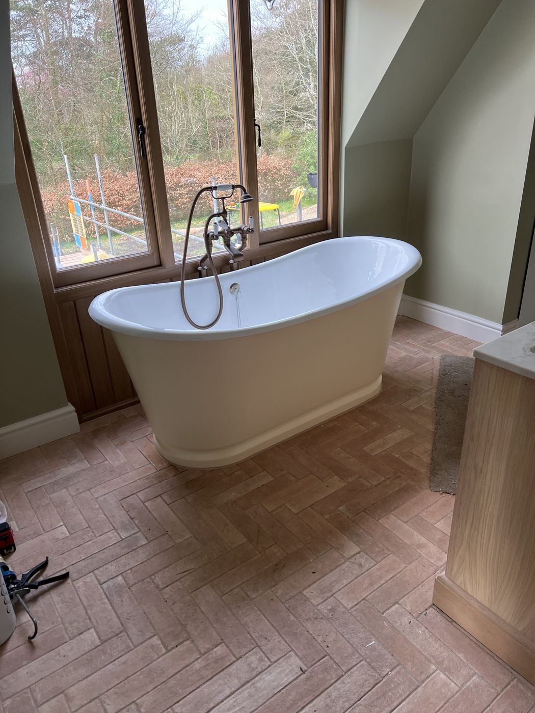 Freestanding bath by the window on a herringbone tile floor