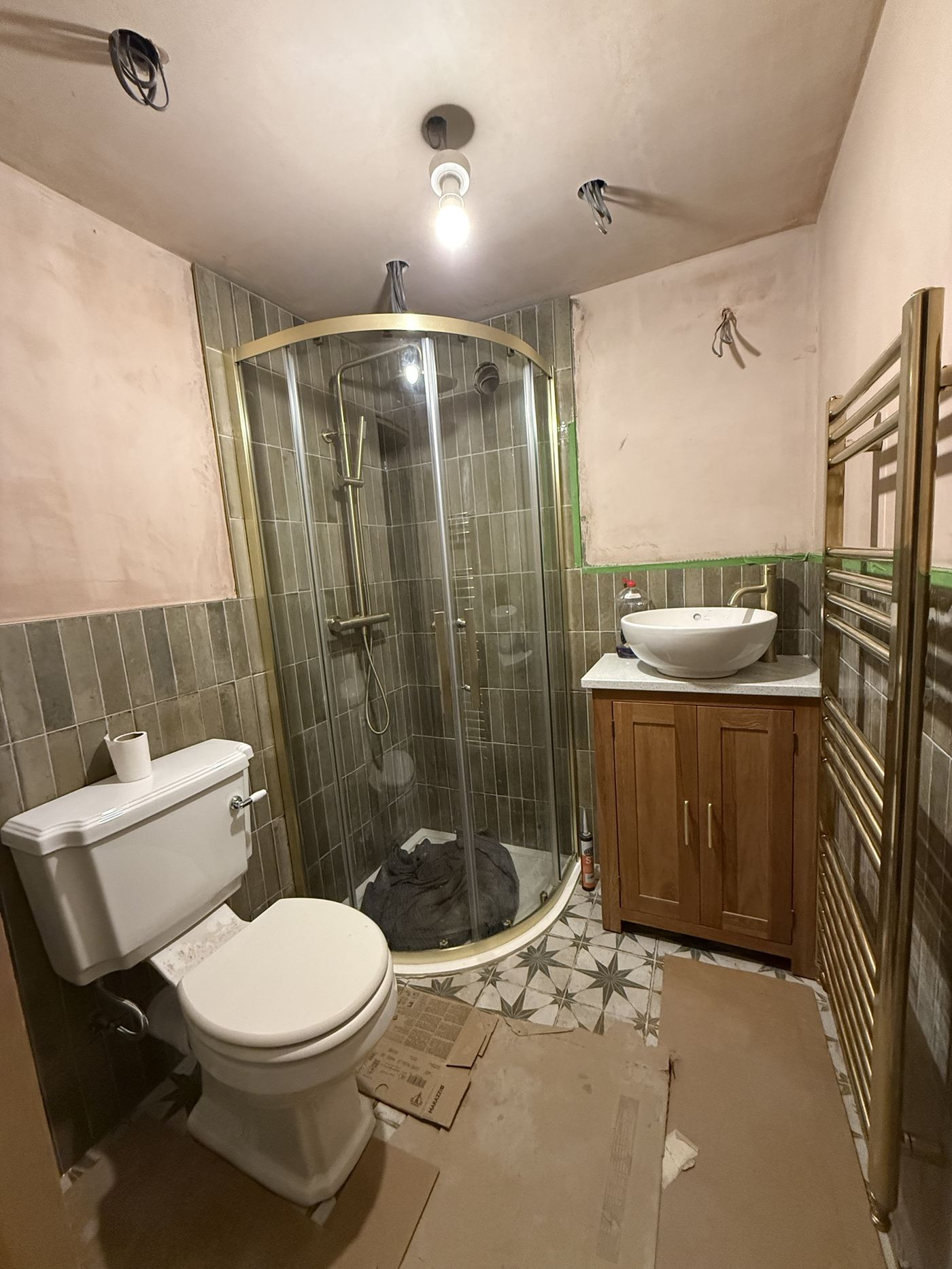 Finished bathroom with green vertical tiles, a brushed brass quadrant shower and towel rail